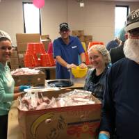 Volunteers smile for a photo while packing food together.